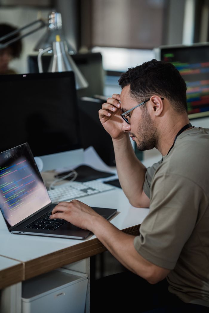 Home A man intensely focused on coding at a desk in a modern office environment.