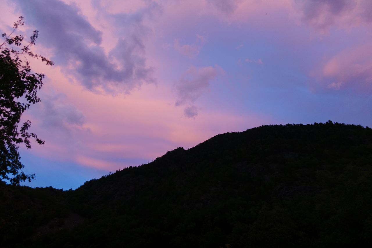 Home A scenic view of hills in silhouette against a vibrant pink and blue sunset sky.