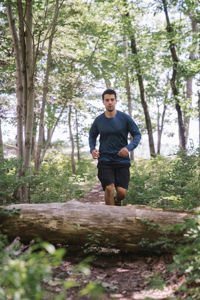 Home A man runs on a forest path, leaping over a large fallen tree trunk. Outdoor fitness.